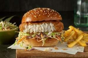 a fish burger with fries on a wooden board