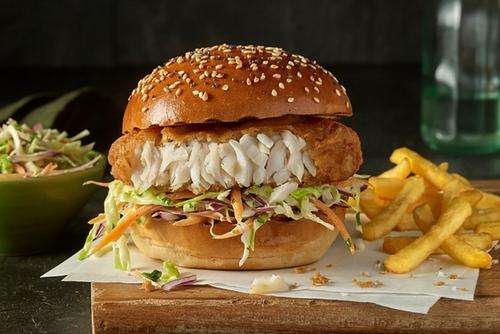 a fish burger with fries on a wooden board